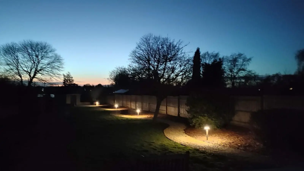 Garden lighting glowing along a lawn and paths at dusk